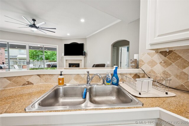 14220 S Vandalia Ave, Bixby, OK 74008 - kitchen featuring arched walkways, a warm lit fireplace, tasteful backsplash, light countertops, and ornamental molding