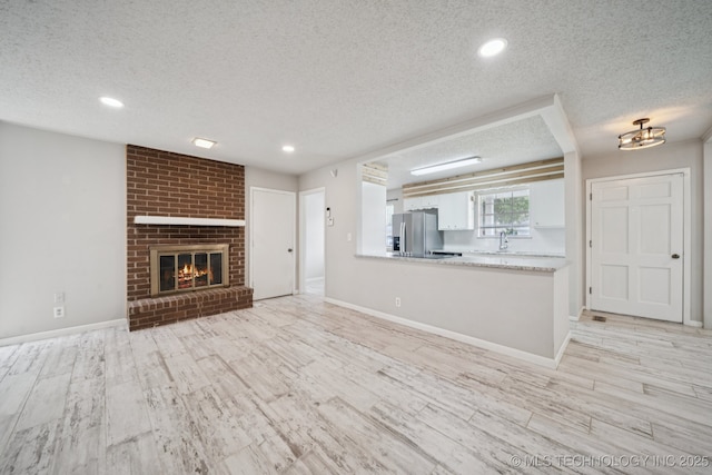 148 E 57th St, Tulsa, OK 74105 - unfurnished living room with a textured ceiling, light wood-style flooring, a brick fireplace, and recessed lighting