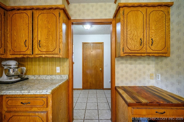 1001 E 1990th Rd, Soper, OK 74759 - kitchen featuring a textured ceiling, wallpapered walls, brown cabinetry, light countertops, and light tile patterned floors