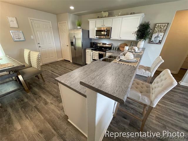 23260 E 115th St S, Broken Arrow, OK 74014 - kitchen featuring appliances with stainless steel finishes, dark wood finished floors, white cabinets, recessed lighting, and a kitchen breakfast bar