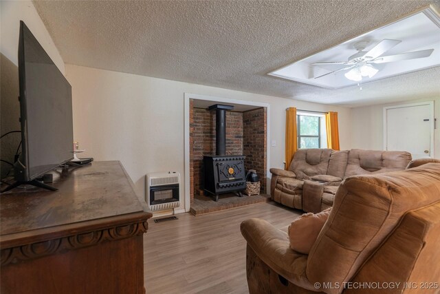 9730 S 4050th Rd, Talala, OK 74080 - living room featuring heating unit, a wood stove, light wood finished floors, a textured ceiling, and a ceiling fan