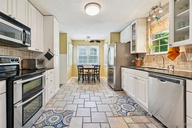 1347 E 37th St, Tulsa, OK 74105 - kitchen featuring stainless steel appliances, stone tile floors, dark countertops, a textured ceiling, and white cabinets