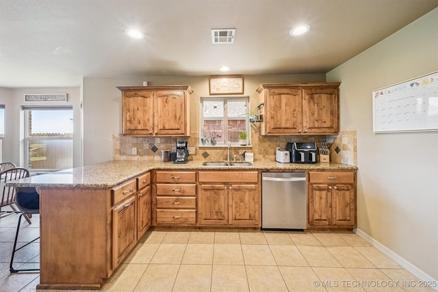 13037 N 124th E Pl, Collinsville, OK 74021 - kitchen with stainless steel dishwasher, a peninsula, backsplash, brown cabinetry, and light stone counters