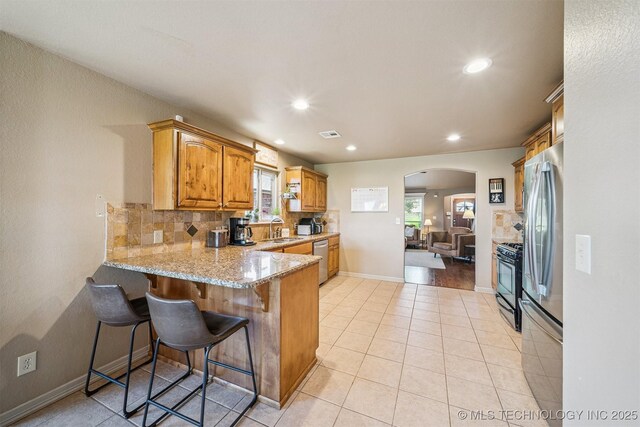 13037 N 124th E Pl, Collinsville, OK 74021 - kitchen featuring arched walkways, a peninsula, appliances with stainless steel finishes, light stone countertops, and decorative backsplash