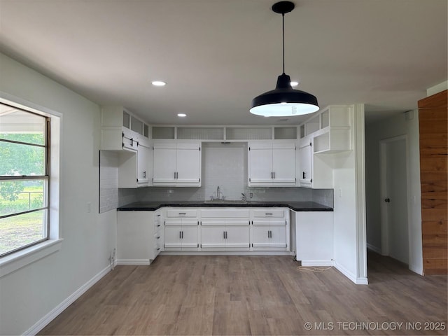 18969 County Road 3560, Ada, OK 74820 - kitchen with dark countertops, light wood-style flooring, backsplash, white cabinetry, and hanging light fixtures