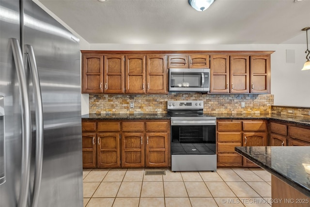 2847 W 115th Pl S, Jenks, OK 74037 - kitchen featuring stainless steel appliances, brown cabinetry, tasteful backsplash, dark stone countertops, and decorative light fixtures