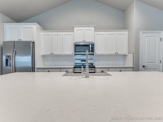 7809 S Redbud Ave, Broken Arrow, OK 74011 - kitchen featuring appliances with stainless steel finishes, vaulted ceiling, tasteful backsplash, white cabinets, and light stone counters