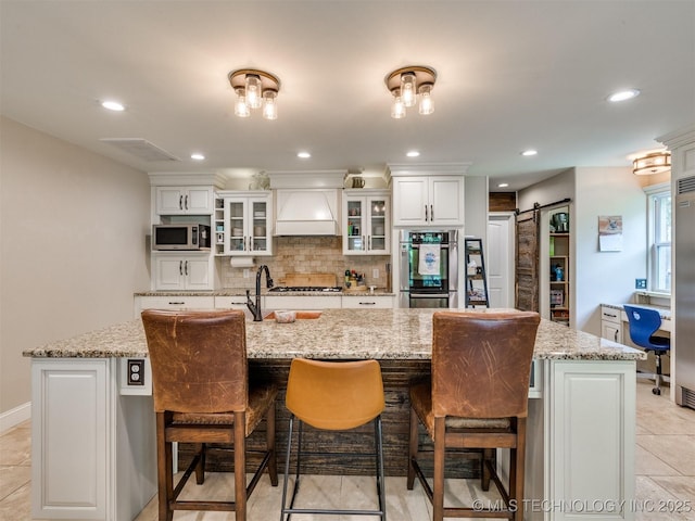 7001 S Redbud Ave, Broken Arrow, OK 74011 - kitchen with stainless steel appliances, custom exhaust hood, tasteful backsplash, a barn door, and an island with sink