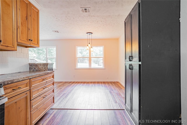11598 E Oak St, Claremore, OK 74019 - kitchen featuring light wood-style flooring, tasteful backsplash, a textured ceiling, brown cabinets, and pendant lighting