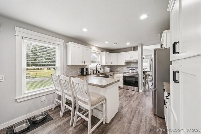 12929 N Sheridan Rd, Collinsville, OK 74021 - kitchen featuring stainless steel appliances, a peninsula, decorative backsplash, white cabinetry, and light wood-style floors