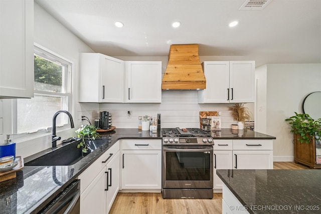 210 NW 4th St, Checotah, OK 74426 - kitchen featuring stainless steel range with gas stovetop, custom exhaust hood, dishwashing machine, light wood-style flooring, and white cabinetry