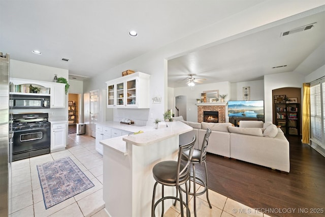 304 S 63rd St, Broken Arrow, OK 74014 - kitchen featuring black appliances, a peninsula, a brick fireplace, a kitchen breakfast bar, and white cabinets