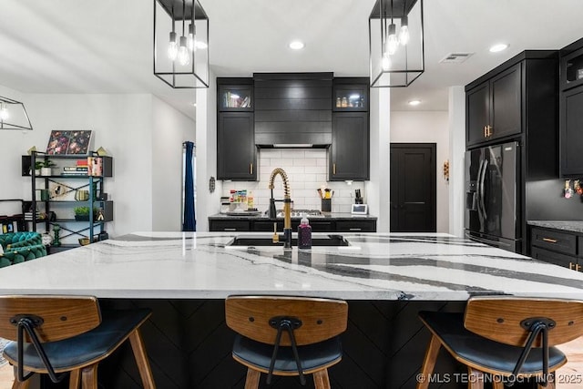 21933 E 101st Pl S, Broken Arrow, OK 74014 - kitchen with refrigerator with ice dispenser, custom exhaust hood, light stone counters, decorative backsplash, and a large island with sink
