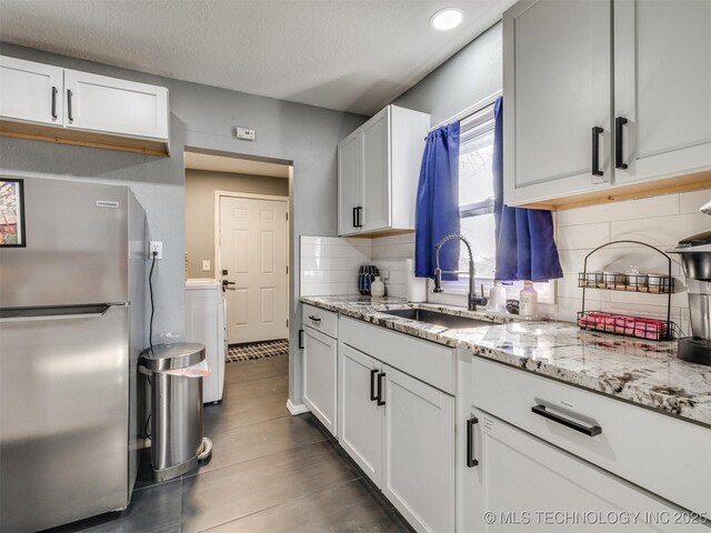 2016 W Easton St, Tulsa, OK 74127 - kitchen featuring freestanding refrigerator, decorative backsplash, washer / dryer, light stone countertops, and a textured ceiling