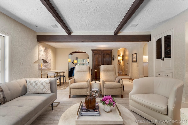 1249 E 26th St, Tulsa, OK 74114 - living room featuring arched walkways, a textured wall, a textured ceiling, beam ceiling, and carpet flooring