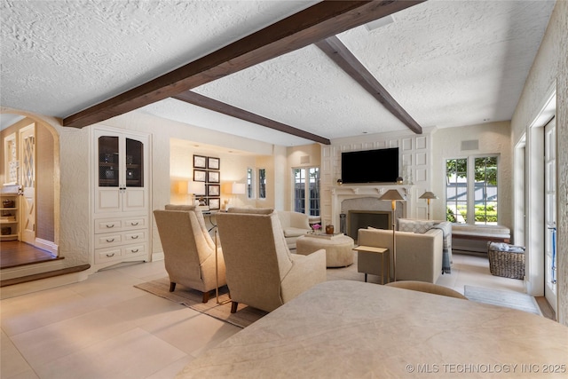 1249 E 26th St, Tulsa, OK 74114 - living area featuring a textured ceiling, beamed ceiling, a fireplace, arched walkways, and light tile patterned floors