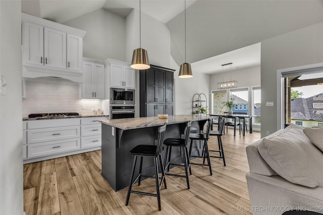 25133 Shade Tree Pl, Claremore, OK 74019 - kitchen with appliances with stainless steel finishes, high vaulted ceiling, a breakfast bar area, backsplash, and white cabinetry