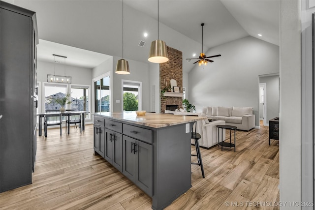 25133 Shade Tree Pl, Claremore, OK 74019 - kitchen with a ceiling fan, high vaulted ceiling, gray cabinets, a kitchen bar, and a brick fireplace