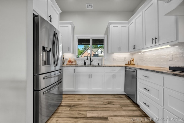 25133 Shade Tree Pl, Claremore, OK 74019 - kitchen featuring stainless steel appliances, white cabinetry, tasteful backsplash, light wood-type flooring, and wall chimney exhaust hood