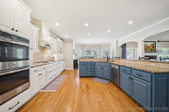 13614 W 42nd Pl, Sand Springs, OK 74063 - kitchen featuring stainless steel appliances, blue cabinetry, arched walkways, white cabinets, and light wood-type flooring