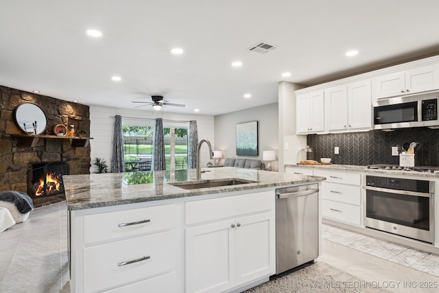 7705 S 232nd E Ave, Broken Arrow, OK 74014 - kitchen with appliances with stainless steel finishes, recessed lighting, an island with sink, light stone countertops, and a stone fireplace