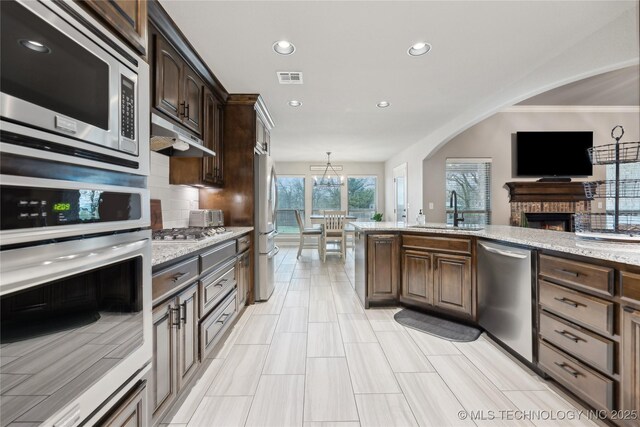 1819 E 43rd St, Sand Springs, OK 74063 - kitchen with appliances with stainless steel finishes, a fireplace, dark brown cabinetry, recessed lighting, and arched walkways