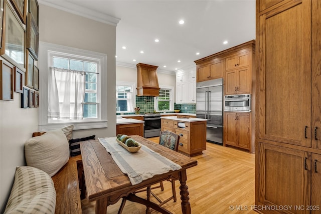 1006 E 17th Pl, Tulsa, OK 74120 - kitchen featuring stainless steel appliances, crown molding, premium range hood, tasteful backsplash, and light wood-type flooring