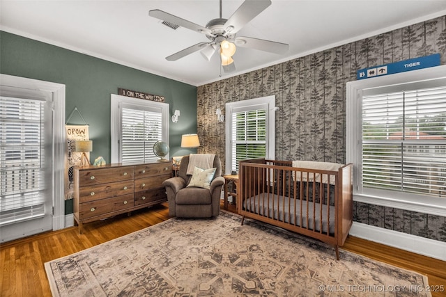 1006 E 17th Pl, Tulsa, OK 74120 - bedroom with wood finished floors, ornamental molding, a crib, wallpapered walls, and a ceiling fan