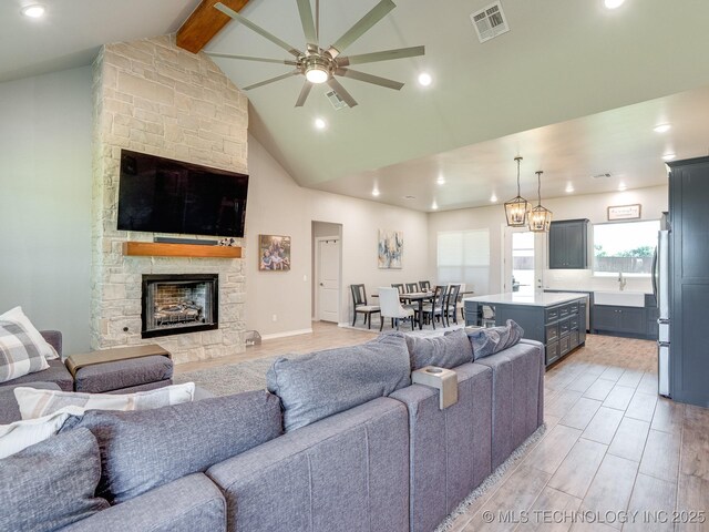 12349 County Road 3571, Ada, OK 74820 - living room featuring ceiling fan, beamed ceiling, a stone fireplace, light wood-style floors, and high vaulted ceiling