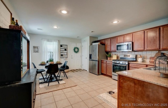 11001 N 146th E Ave, Owasso, OK 74055 - kitchen with stainless steel appliances, decorative backsplash, recessed lighting, brown cabinetry, and light stone countertops