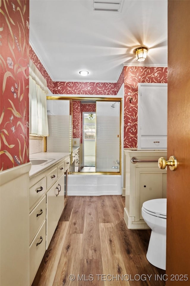 5153 S Marion Ave, Tulsa, OK 74135 - bathroom with wallpapered walls, crown molding, vanity, bath / shower combo with glass door, and wood finished floors