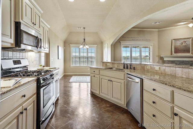1854 E 137th Pl, Glenpool, OK 74033 - kitchen with stainless steel appliances, cream cabinetry, decorative backsplash, arched walkways, and vaulted ceiling