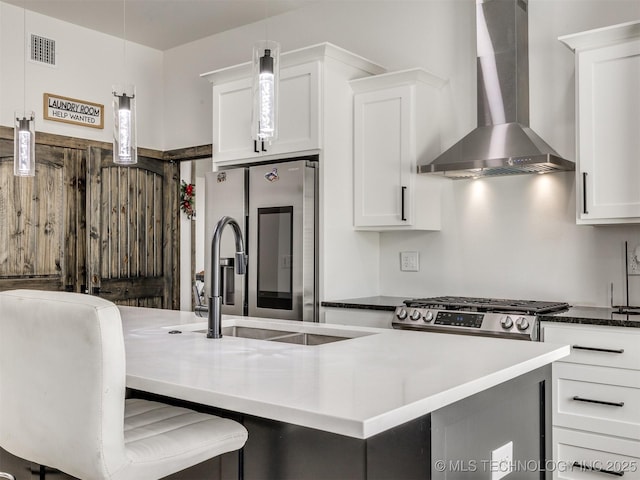 11446 Mary Knox Dr, Beggs, OK 74421 - kitchen featuring wall chimney range hood, appliances with stainless steel finishes, white cabinets, hanging light fixtures, and a kitchen island with sink