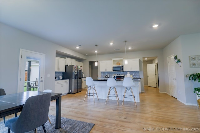 9516 E 131st Pl S, Bixby, OK 74008 - kitchen with stainless steel appliances, tasteful backsplash, white cabinetry, a kitchen breakfast bar, and light wood-style flooring