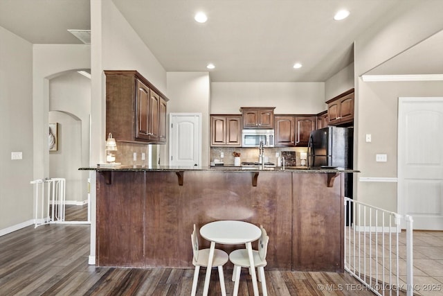 1801 E Montgomery St, Broken Arrow, OK 74012 - kitchen with stainless steel microwave, freestanding refrigerator, arched walkways, a breakfast bar, and backsplash
