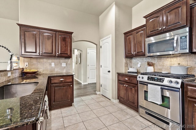 1801 E Montgomery St, Broken Arrow, OK 74012 - kitchen featuring appliances with stainless steel finishes, dark stone countertops, decorative backsplash, light tile patterned flooring, and arched walkways