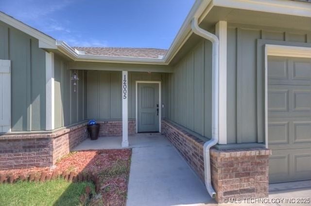 12005 E 108th Pl N, Owasso, OK 74055 - doorway to property with brick siding, a garage, board and batten siding, and covered porch