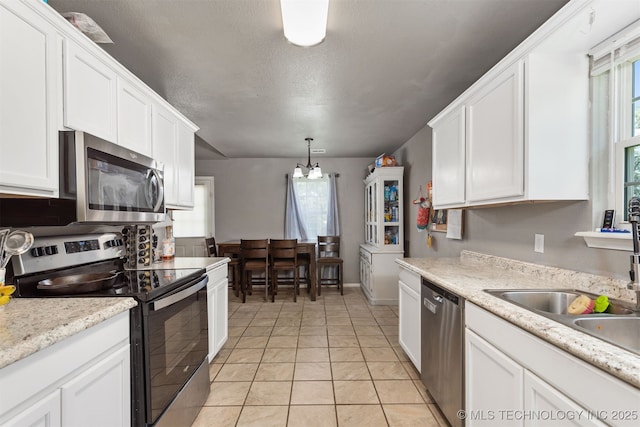 802 NE 9th St, Wagoner, OK 74467 - kitchen with appliances with stainless steel finishes, white cabinetry, light tile patterned floors, healthy amount of natural light, and a textured ceiling