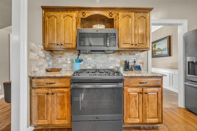 13804 E 90th St, Owasso, OK 74055 - kitchen featuring stainless steel appliances, wood finished floors, light stone countertops, backsplash, and a wainscoted wall