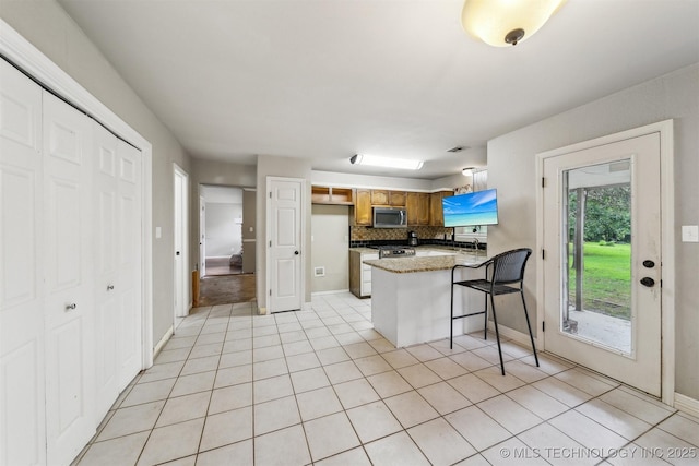 8973 N Crestwood Dr, Sperry, OK 74073 - kitchen with stainless steel appliances, a peninsula, light tile patterned flooring, decorative backsplash, and a kitchen bar
