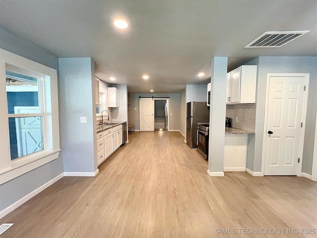 609 E Ward St, Tahlequah, OK 74464 - kitchen featuring a barn door, light wood-style flooring, white cabinets, appliances with stainless steel finishes, and tasteful backsplash