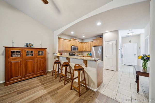 445 S Cypress Ave, Broken Arrow, OK 74012 - kitchen featuring stainless steel appliances, a peninsula, light stone countertops, a kitchen bar, and arched walkways