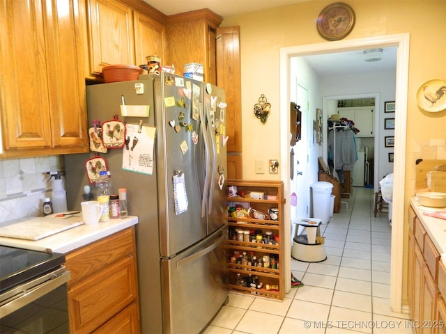 399987 W 3700th Rd, Ramona, OK 74061 - kitchen with light tile patterned flooring, freestanding refrigerator, backsplash, light countertops, and brown cabinetry