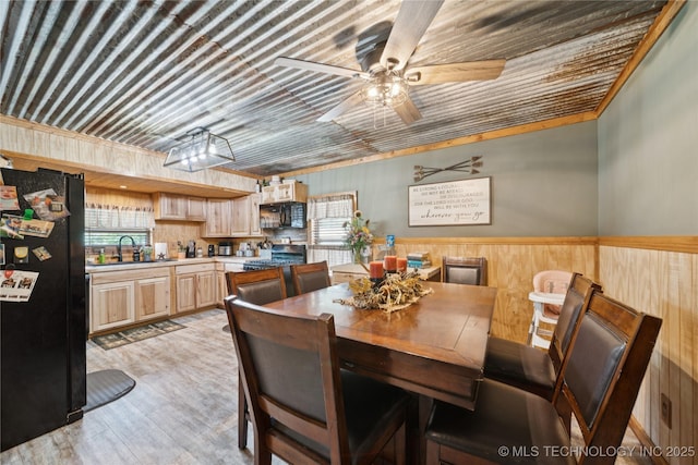 719 Oklahoma Ave, Wynona, OK 74084 - dining space with wooden walls, light wood-style flooring, a ceiling fan, and a wainscoted wall