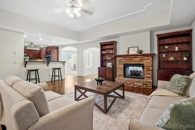 13718 S 262nd E Ave, Coweta, OK 74429 - living room featuring ceiling fan, arched walkways, a raised ceiling, light wood-type flooring, and a brick fireplace