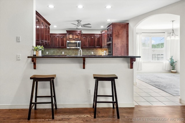 13718 S 262nd E Ave, Coweta, OK 74429 - kitchen featuring appliances with stainless steel finishes, dark countertops, ceiling fan, a kitchen breakfast bar, and arched walkways
