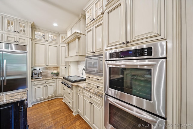 19735 E Woodhaven Rd, Owasso, OK 74055 - kitchen featuring built in appliances, cream cabinetry, backsplash, light stone counters, and light wood finished floors
