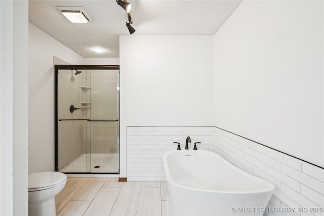 7222 E 87th St, Tulsa, OK 74133 - full bathroom featuring tile walls, a freestanding tub, a stall shower, a textured ceiling, and a wainscoted wall