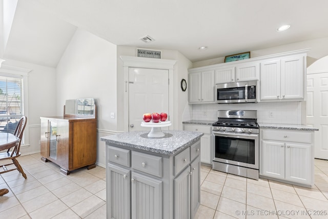 1014 W 120th St S, Jenks, OK 74037 - kitchen with appliances with stainless steel finishes, decorative backsplash, light tile patterned flooring, vaulted ceiling, and a center island