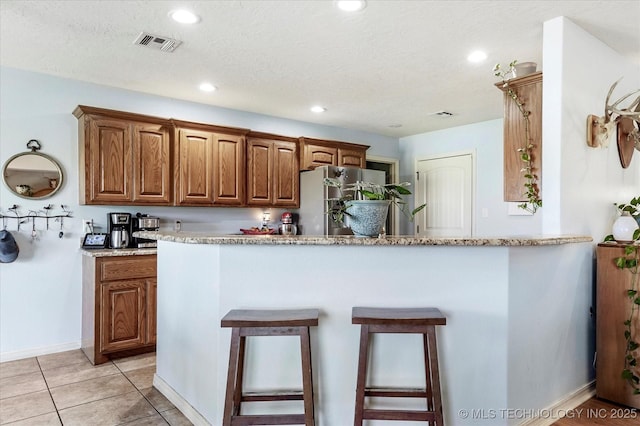 545 E 498th Cir, Pryor, OK 74361 - kitchen featuring freestanding refrigerator, brown cabinets, a kitchen breakfast bar, recessed lighting, and light stone countertops